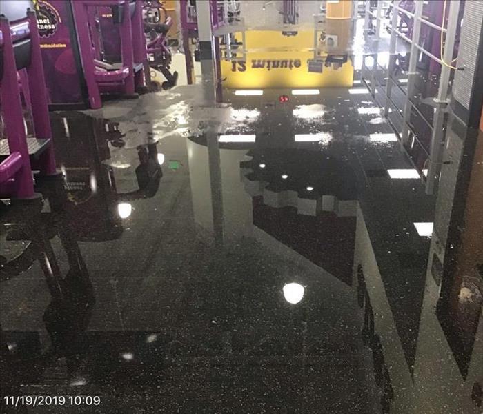 Flooded gym floor, with reflections of the equipment on the water.
